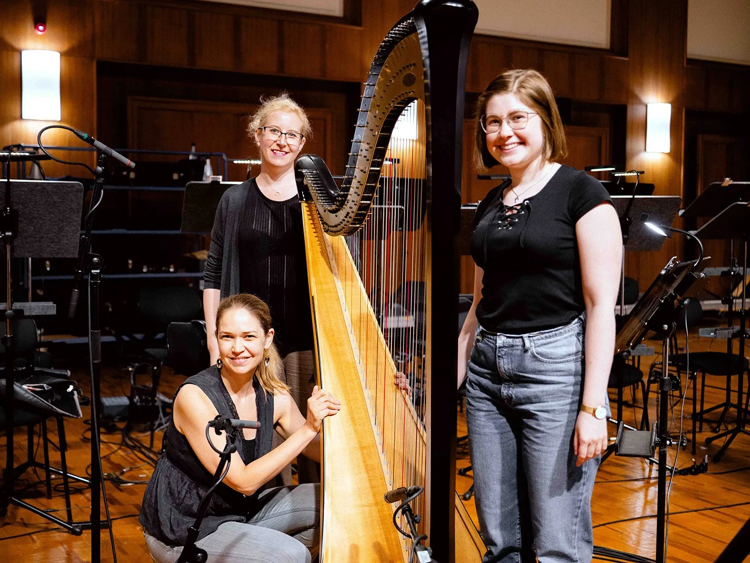 Three BBO Harps musicians posing beside a concert harp at Vienna Synchron Stage.