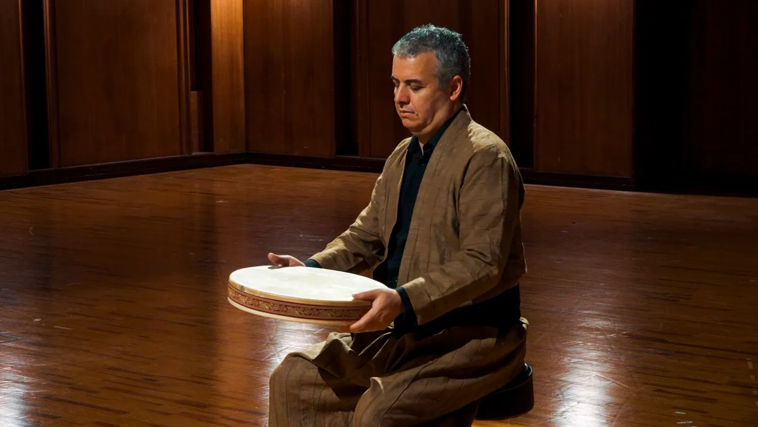 Seated percussionist holding a frame drum horizontally at Vienna Synchron Stage
